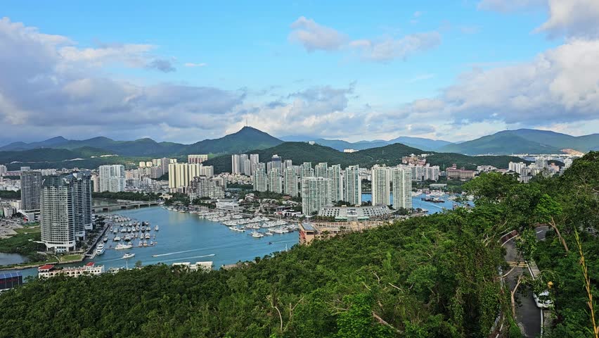 Scenic panoramic view of Sanya from Deer Turned Head Park, featuring a modern skyline, marina, mountains, lush greenery, and waterfront under a bright tropical sky.