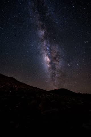 A bright Milky Way stretches across the night sky above a rocky volcanic slope on Maui, revealing countless stars over the dark landscape.