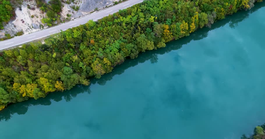 Aerial top-down view of a van driving on a road between a mountain and a beautiful river