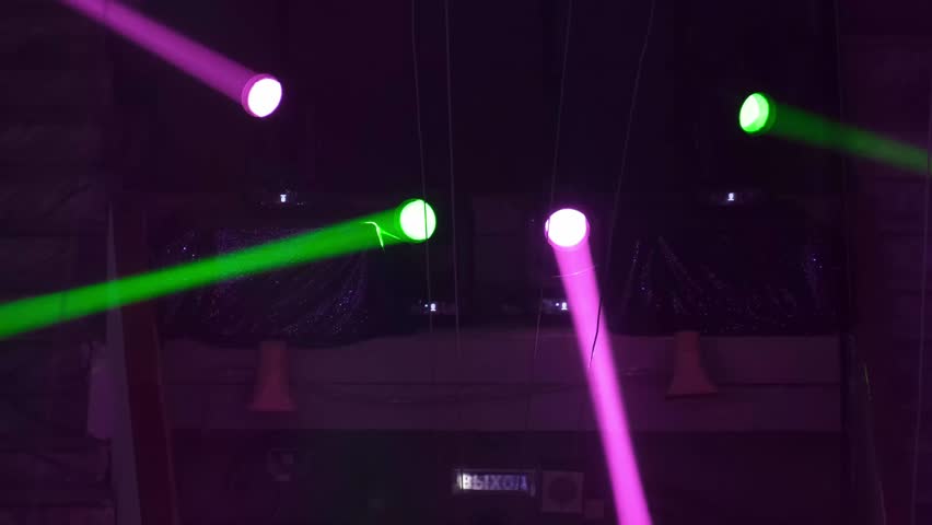 Bright moving stage lights project vivid green and magenta beams across a dark concert hall, capturing the energy of live shows, modern lighting design and entertainment technology