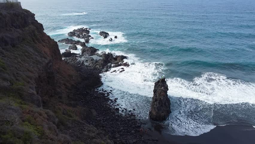 drone Aerial view of Playa El Bollullo’s rocky coastline and black sand, capturing dramatic waves crashing against the volcanic rock formations in Tenerife	
