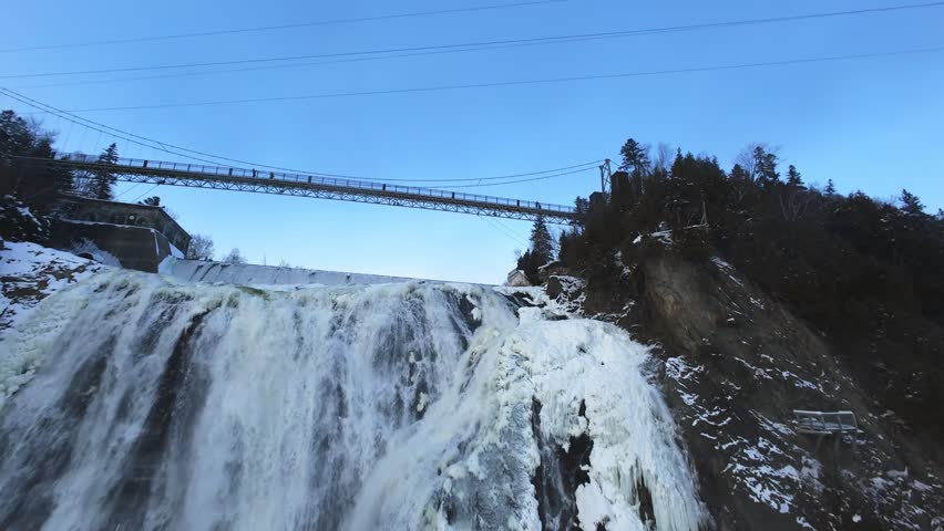 Cinematic aerial view of a frozen river and snowy waterfall in winter. Cold season nature, icy water surface and dramatic cliffs captured by drone.