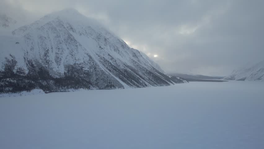 Aerial moves towards snowy shore, crossing vast, frozen Kathleen Lake moving towards majestic King