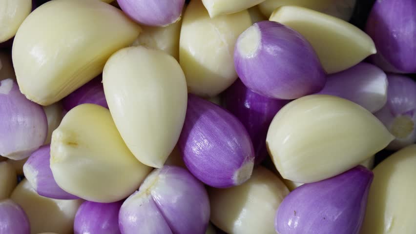 Rotating pile of peeled red onion and garlic in top view. Fresh bulbs highlight texture, flavor, and serve as essential ingredient