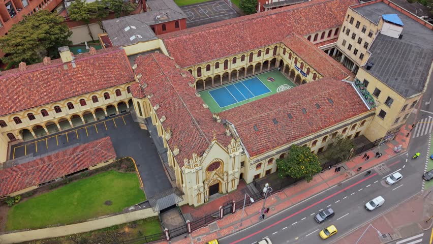 Drone pullback revealing a yellow school complex in Bogotá with its courtyard and street.