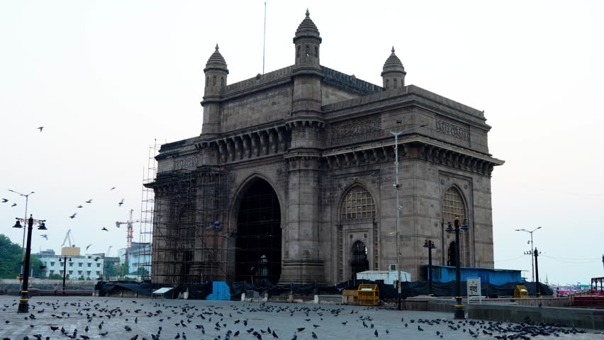 Early morning view of the Gateway of India in Mumbai with restoration scaffolding, flying pigeons, calm atmosphere, and soft sunrise light capturing iconic architecture and peaceful urban moments.