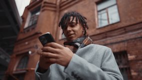 Joyful black guy chatting online in mobile app, portrait of man with smartphone. Townsman walking down city street in autumn or winter season, good mood and positive motion, cybersecurity in internet - Powered by Shutterstock - Get 15% off with code: PIKWIZARD15