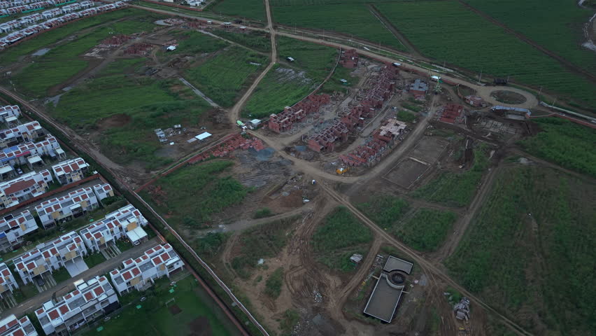 Drone footage captures a sprawling construction site in Valle del Cauca, Colombia, showcasing an intricate layout of developing structures amidst lush green fields under soft lighting.