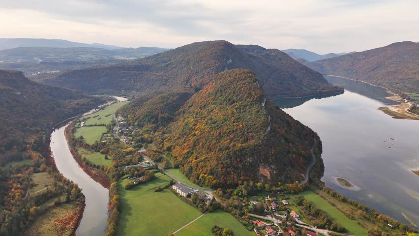 Aerial view of Belvedere lac de Coiselet in France with a winding river, autumn colored hills, calm lake waters and a rural valley landscape surrounded by forests and houses beneath rolling mountains