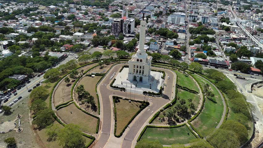 Aerial drone view of the Monument to the Heroes of the Restoration. The iconic white landmark tower sits atop a hill overlooking the city of Santiago de los Caballeros in the Dominican Republic