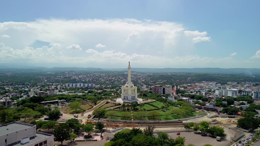 Aerial drone view of the Monument to the Heroes of the Restoration in Santiago. The white tower stands on a green hill with the city in the background under a blue sky