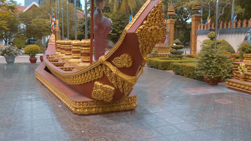 A statue of a monk with a begging bowl under the parasol standing on a boat in the garden of Wat Preah Prom Rath Buddhist temple in Siem Reap, Cambodia. Shot in motion