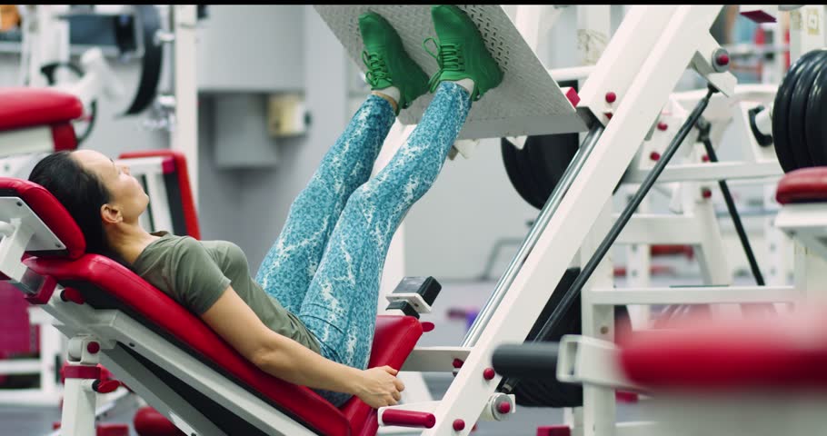 A middle-aged Caucasian woman trains her leg muscles with the leg press machine. She using the leg press, maintaining proper form and steady pace to maximize muscle engagement in the gym.