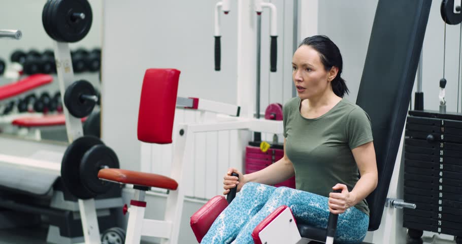 Gym workout. A middle-aged woman trains her leg muscles with the leg abduction machine, focusing on controlled, powerful movements during her gym workout. 4k footage.