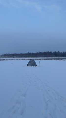 A fishing tent with an ice drill stands on the ice of a lake in the forest of Yakutia.