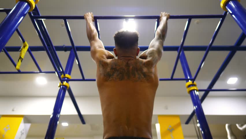 Muscular afro american athlete doing pull ups at modern gym. Young african sportsman exercising on horizontal bar. Strong sporty man training at sport club. Healthy and active lifestyle concept