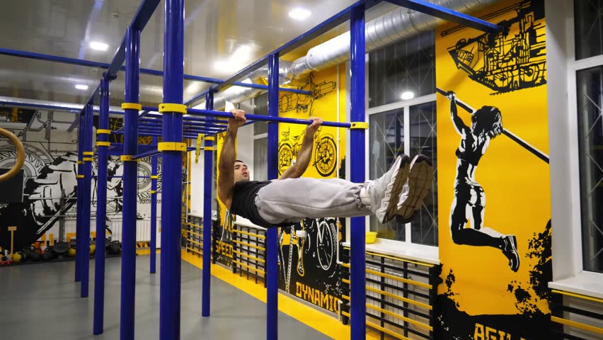 Young muscular athlete showing some gymnastics stunts on horizontal bar at sport club. Strong sporty man performing static exercises during workout at modern gym. Concept of sportive lifestyle
