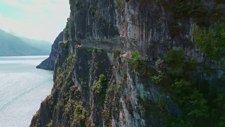 Aerial view of the picturesque Ponale trail in Garda Trentino, winding sheer above Lake Garda in the Italian Alps, with hikers and cyclists traveling this iconic alpine path.