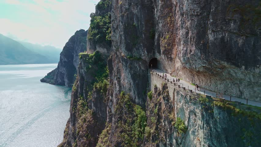 Aerial view of the picturesque Ponale trail in Garda Trentino, winding sheer above Lake Garda in the Italian Alps, with hikers and cyclists traveling this iconic alpine path.