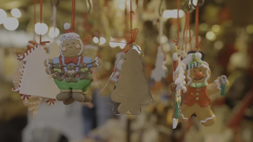 Handcrafted clay gingerbread-style ornaments shaped like snowmen, Santas, and cookie figures hanging inside a wooden Christmas market stall. Cozy artisan holiday decor