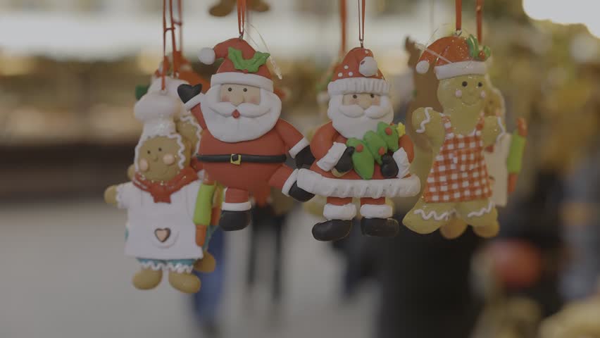 Handcrafted clay gingerbread-style ornaments shaped like snowmen, Santas, and cookie figures hanging inside a wooden Christmas market stall. Cozy artisan holiday decor