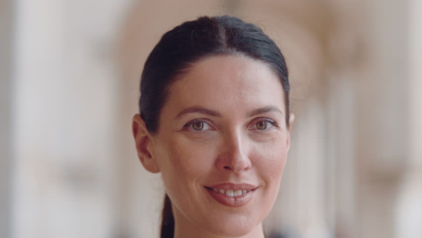 Closeup portrait of smiling woman with natural makeup and tied hair standing in bright corridor showing calm expression and confidence with blurred background