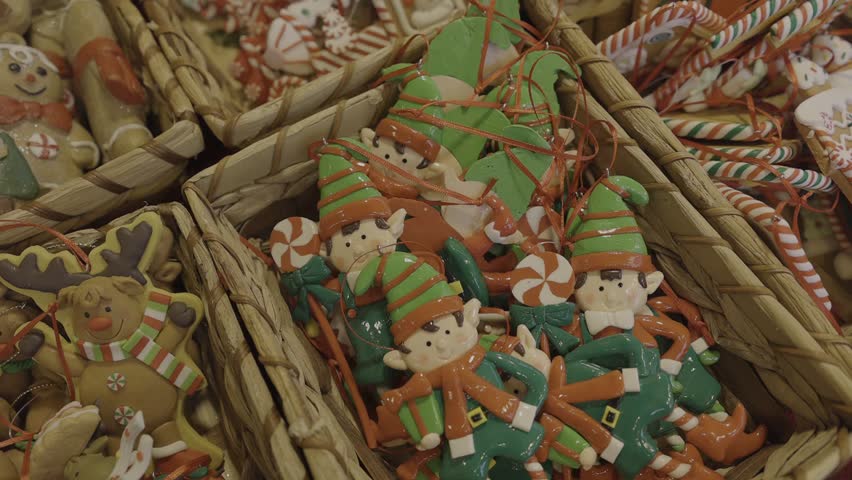 Handcrafted clay gingerbread-style ornaments shaped like snowmen, Santas, and cookie figures displayed in boxes inside a wooden Christmas market stall. Cozy artisan holiday decor