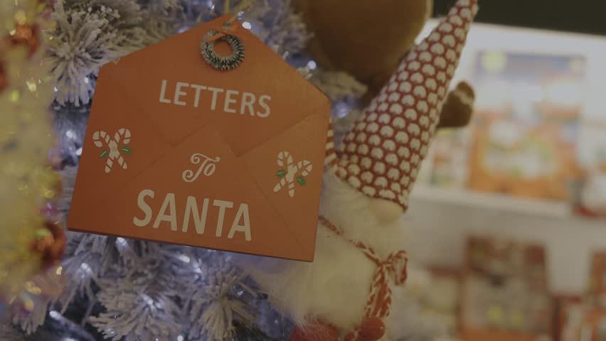 White artificial Christmas tree decorated with twinkling garland and a wooden Letters to Santa sign shaped like a red mailbox with a small elf. Cozy festive holiday scene