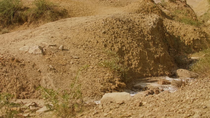 Revealing shot of a human representation of Christ in traditional biblical-style clothing, walking through an arid desert landscape, surrounded by sculpted sand formations and warm golden light. Cinematic scene evoking solitude, spirituality and timeless exploration. Christian concept. Slow motion shot