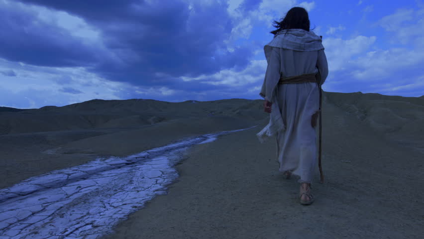 The solitary figure of the Messiah, wearing ancient robe, walks away into the night, crossing a barren and rugged landscape. A dry white stream runs through the foreground, against a dramatic blue sky, emphasizing the isolation of the spiritual journey.