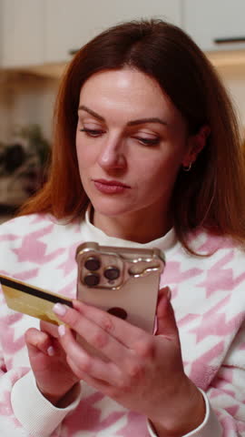 Middle-aged woman at night home pays online order with smartphone and credit card smiles after approval. Caucasian girl on sofa at evening confirms purchase checks payment status ecommerce checkout
