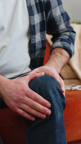 Unrecognizable middle-aged man suffer from painful discomfort severe knee joint ache leg muscles could not walk. Sick guy massaging knees illness cramps rheumatism at home on sofa. Health care problem