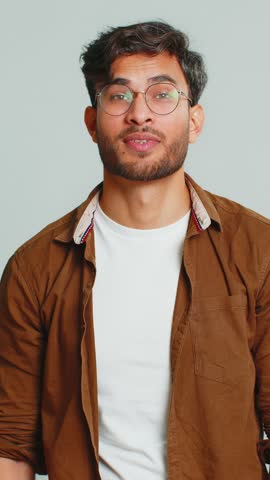 Need some more, please give me. Indian man showing a little bit gesture with sceptic smile showing minimum sign, measuring small size, begging help. Arabian guy isolated on gray studio background