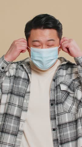 Asian middle-aged man happily removing, taking off medical mask and throws it away. Flu treatment cure. Ending of pandemic quarantine, recover after contagious disease. Chinese guy on beige background