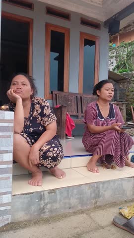 Candid shot of two women on a house porch in rural Indonesia. Representing genuine Asian local culture, social interaction, and typical village ambiance. Excellent for documentary or travel marketing.