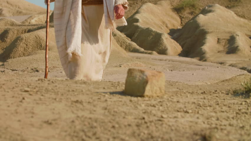 A wanderer in ancient-style clothing stepping across a dusty desert path. Christian and spiritual concept. Slow motion Shot