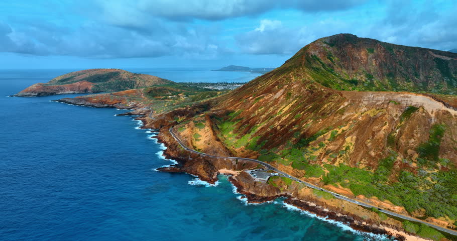 View on the Diamond Head Crater from above the waterscape of the Pacific Ocean. A modern highway passes at the foot of the volcanic rock along the rocky coast. Heavy cloudscape at the backdrop. Honolulu, Hawaii, USA.
