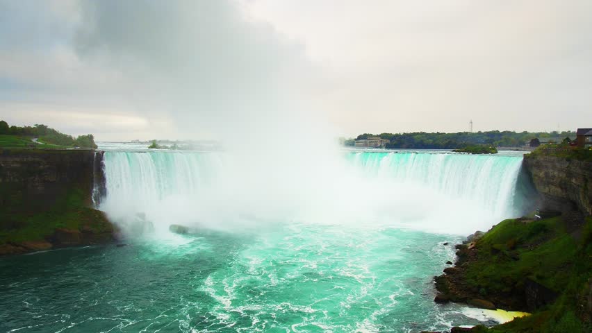 Niagara Falls. Aerial view of Niagara Falls with misty waterfalls and rocky cliffs against a cloudy sky.