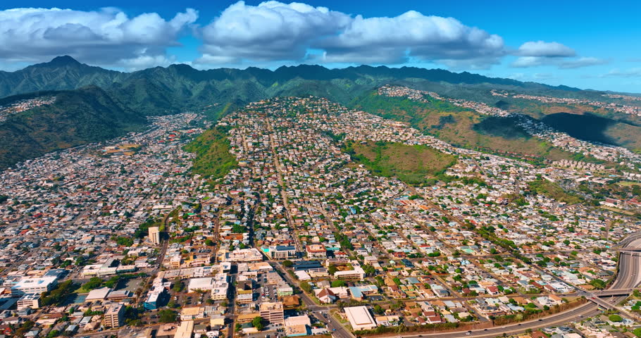 Sunny scenery of densely built urban area of modern Honolulu, Hawaii, USA. Amazing green mountain ranges under the heavy cloudscape at the backdrop. Aerial view.