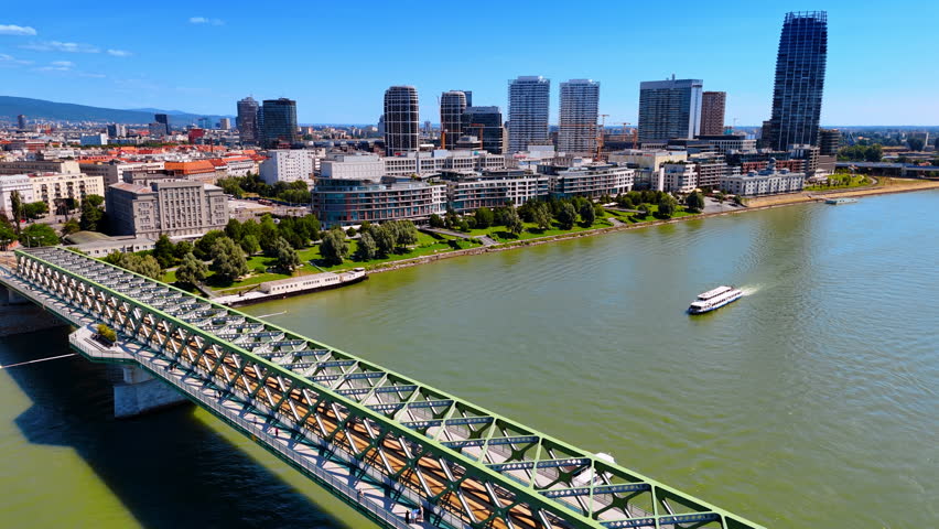 Boats move under the old bridge by the Danube. Modern skyline on the waterfront at backdrop. Bratislava, Slovakia.