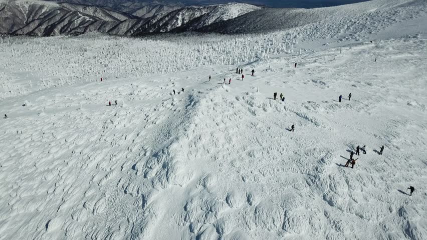 Tourists play on the snowy mountaintop and cable cars fly over Juhyo forests (ice trees, snow monsters), with snow covered mountains on the horizon, in Zao hot spring and ski resort, Yamagata, Japan