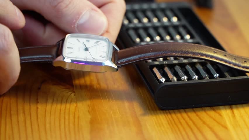 close up of a mans hand turning the crown of a classic silver wristwatch with a brown leather strap to set the time accurately symbolizing precision maintenance work and punctuality