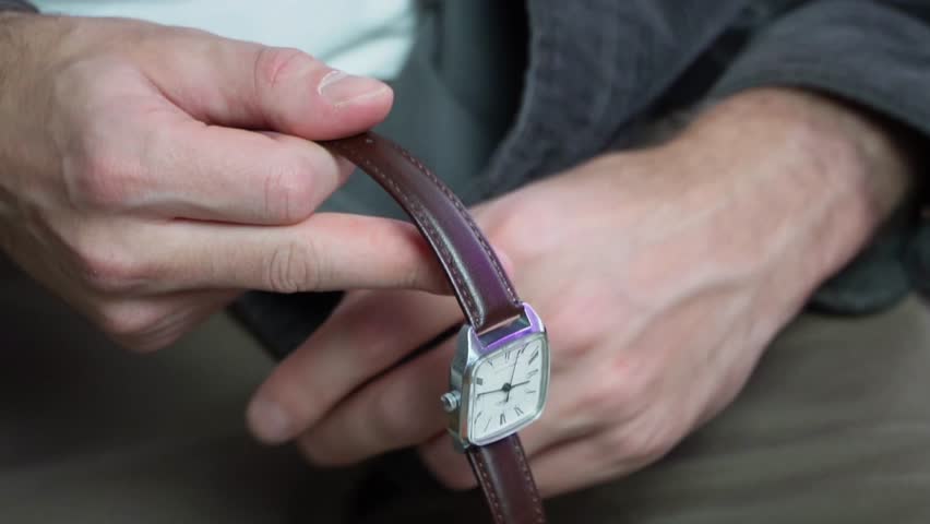 close up of a man fastening the brown leather strap of a classic silver wristwatch onto his wrist symbolizing daily routine morning preparations style fashion and punctuality video footage