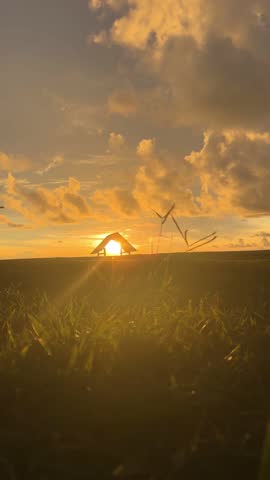 Footage 4g, silhouette of a gazebo on a grassy field during a dramatic golden sunset with beautiful clouds and sun rays.
