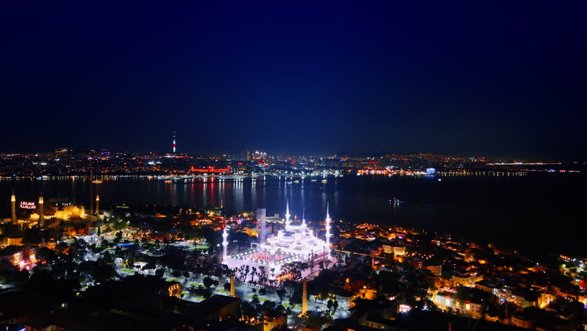 Stunning illumination of mosques in the night scenery of Istanbul, Turkey. Boat with lights moves by the waterscape. Aerial view.