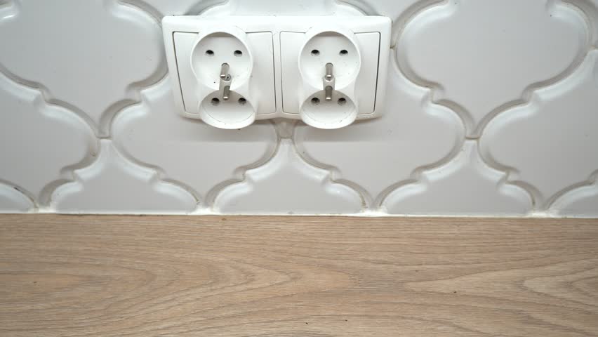 Two electrical outlets are mounted on a white tile wall above a wooden countertop, providing power
