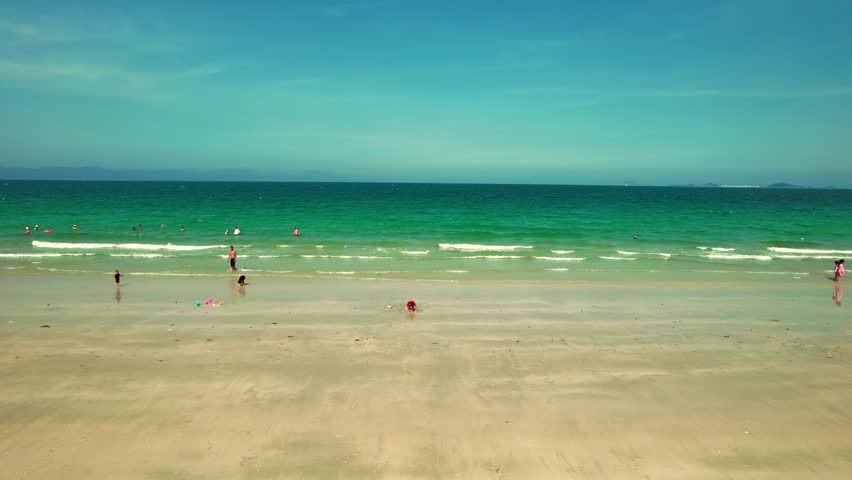 Low aerial tracking shot flying horizontally along the pristine Doc Let beach, Nha Trang, Vietnam. Vivid turquoise water and bright summer sunshine create a perfect tropical vacation vibe.
