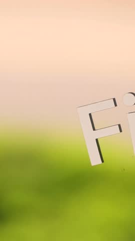 The word FITNESS is applied on transparent glass, creating a logo effect. Behind the glass, bright green grass reflects softly in bokeh, making the white letters stand out for modern design use.