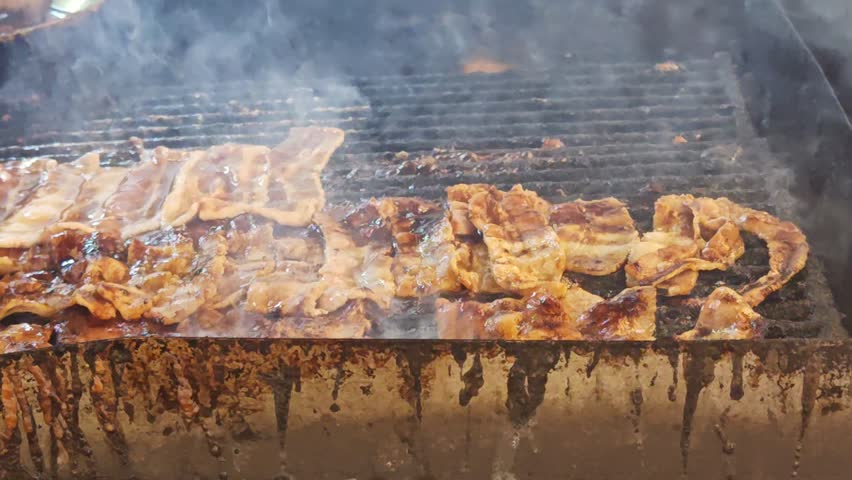 Juicy pork ribs sizzle on a smoky outdoor grill as a chef wearing gloves handles the meat. Char marks, dripping fat, and rising steam convey a savory barbecue scene full of flavor and aroma.