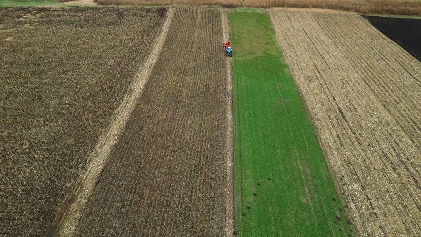 Aerial 4K top down view of tractor on farmland field strips